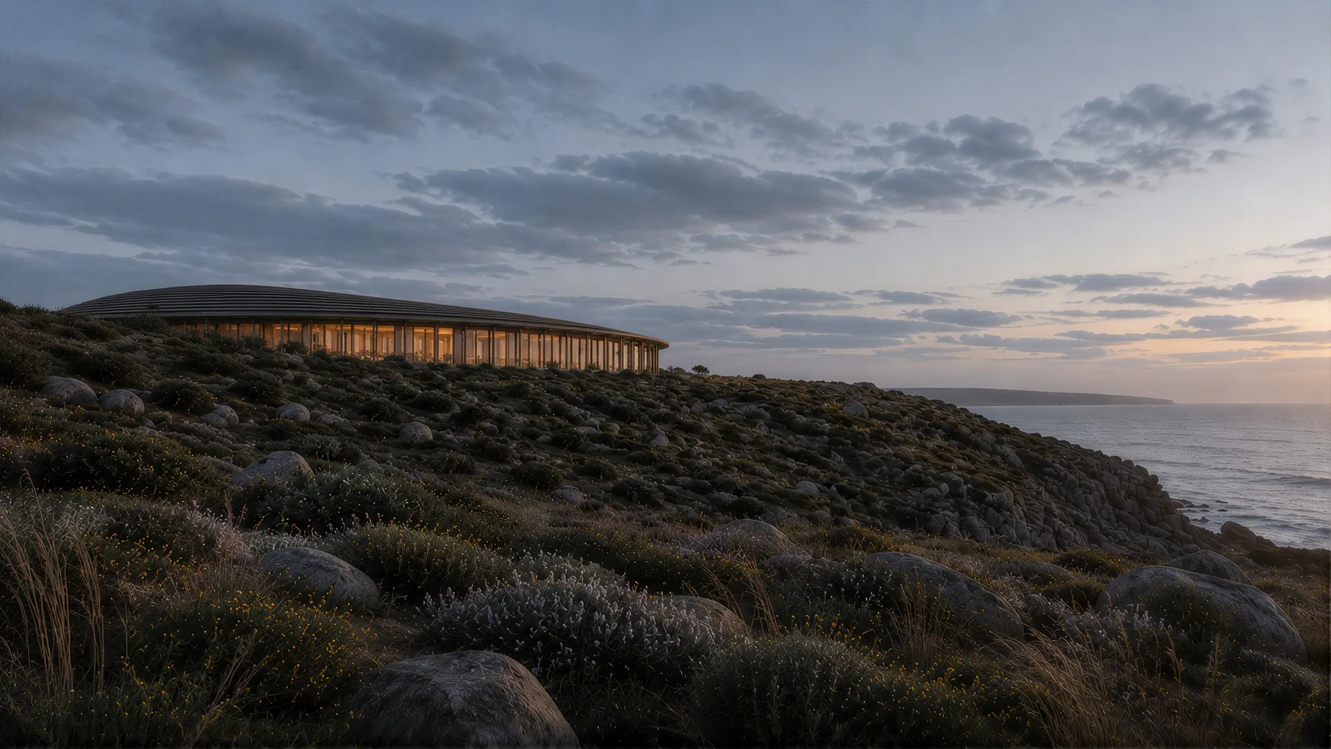 The low building lit at dusk on the headland above the sea