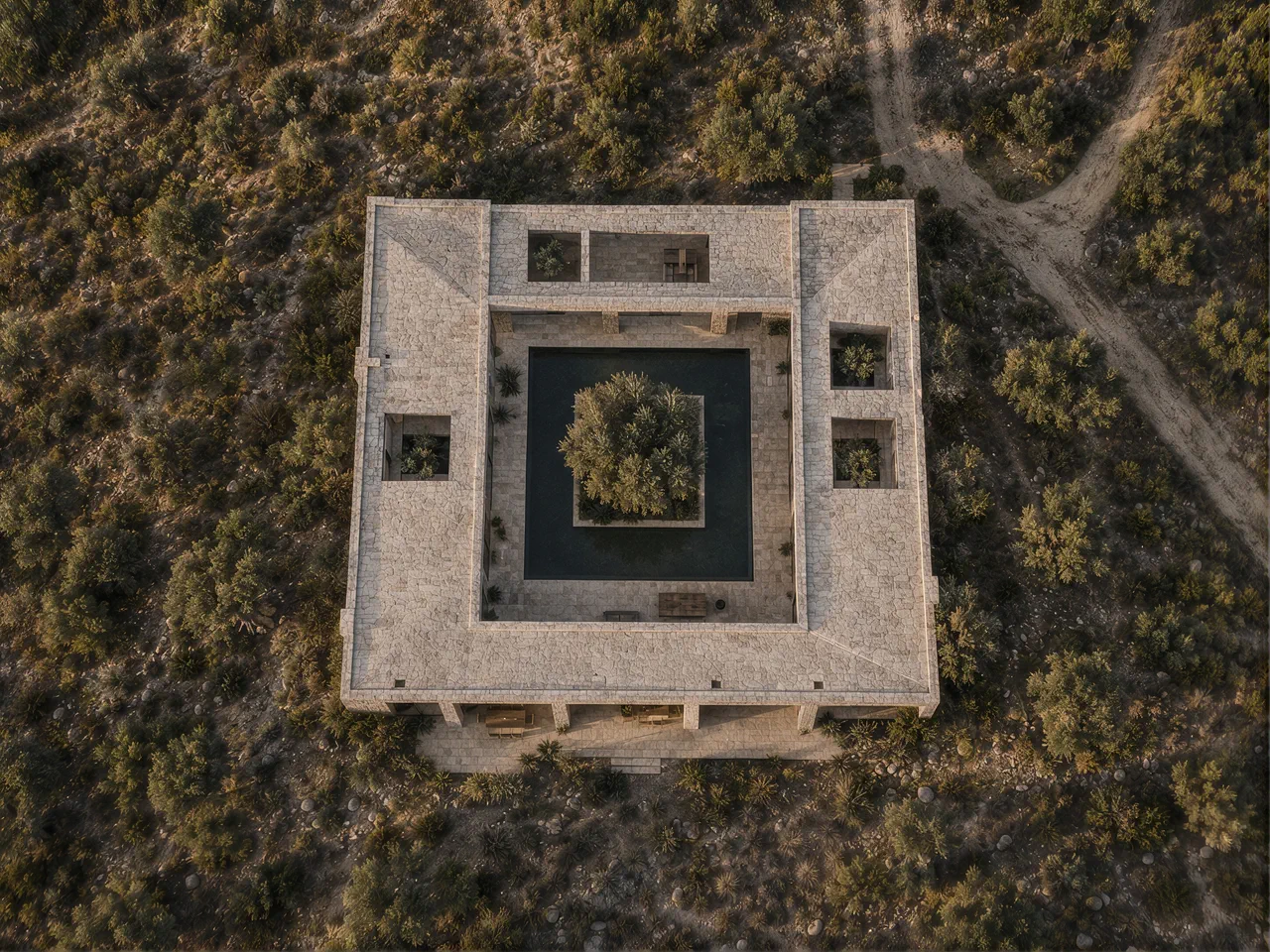 Aerial view of a square stone courtyard house surrounded by dry scrubland