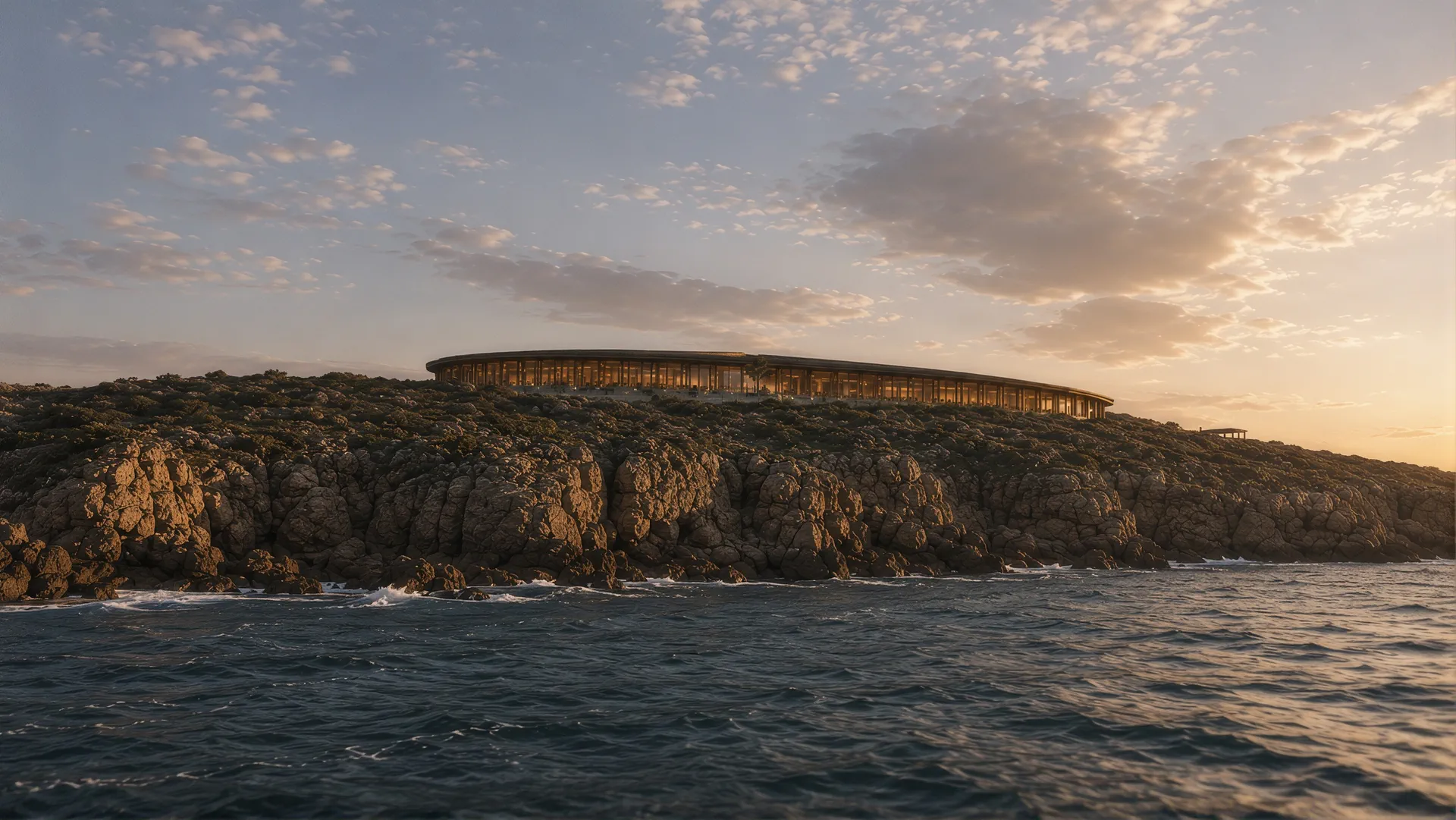 A low ring-shaped building on a rocky headland above the Atlantic at sunset
